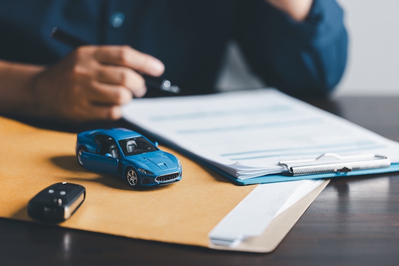 Businesswoman signing car insurance document or lease paper. Writing signature on contract or agreement. Buying or selling new or used vehicle. Car keys on table. Warranty or guarantee.