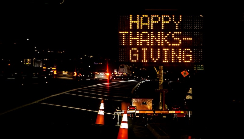An electronic freeway sign stating Happy Thanksgiving with traffic in the background