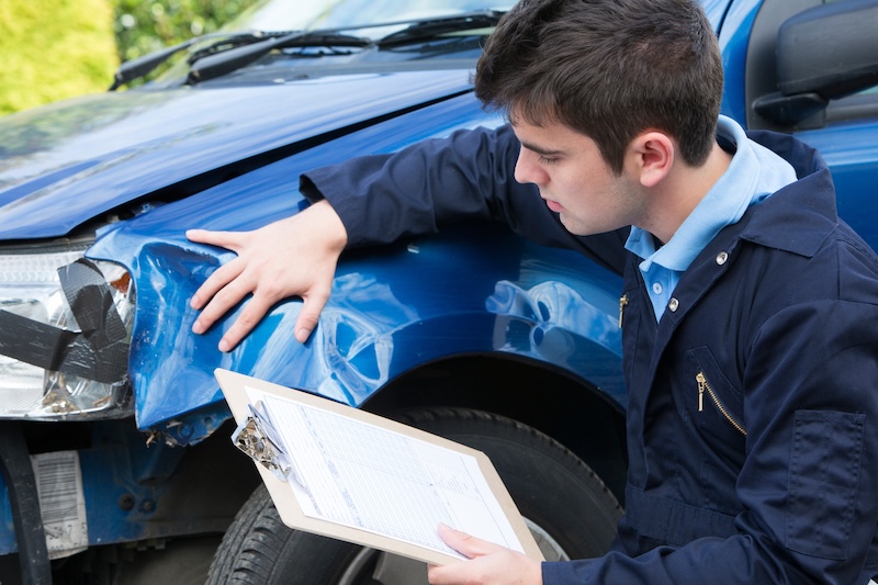 Auto Workshop Mechanic Inspecting Damage To Car And Filling In Repair Estimate