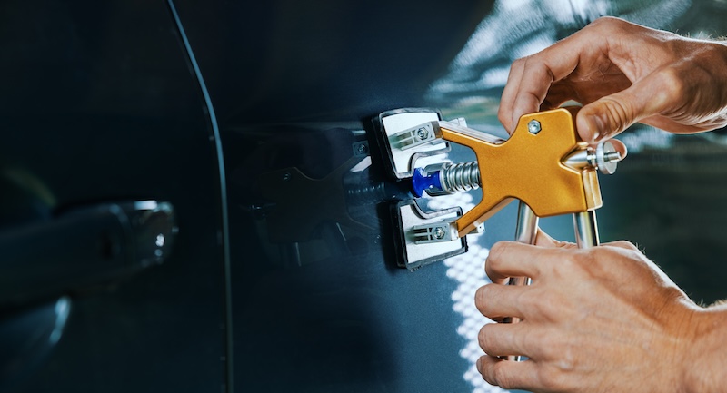 paintless car dent repair. man fixing vehicle door with PDR technology tool