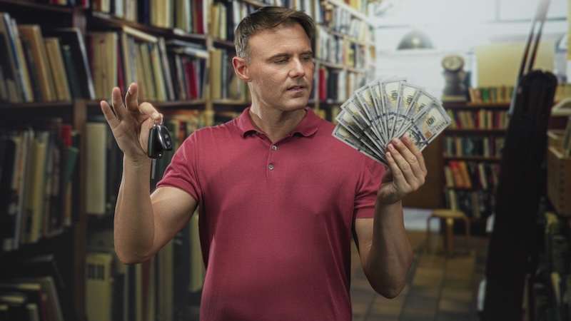 Man holding car keys in one hand and fanning a stack of us dollars with the other in a bookshop building; temptation decision confidence.
