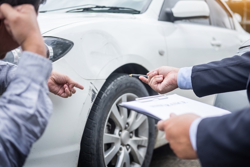 Insurance agent writing on clipboard while examining car after accident claim being assessed and processed