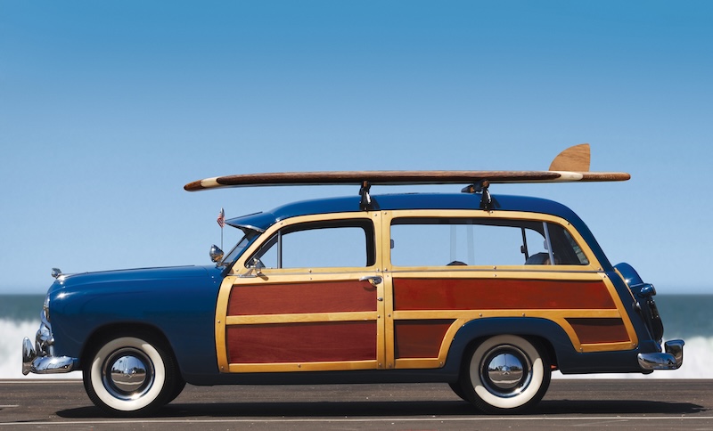 side view of woody car with surfboard and surf in background