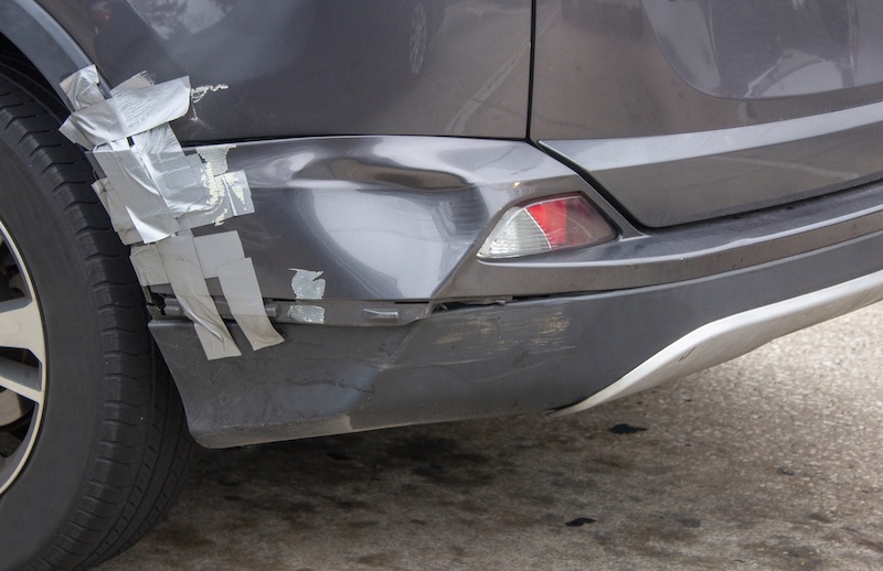 a gray car with a dented rear bumper that is held together with duct tape