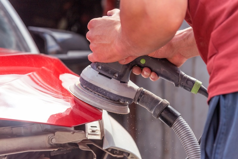 Grinder in the hands of a man who sharpen a car varnish in the car shop.