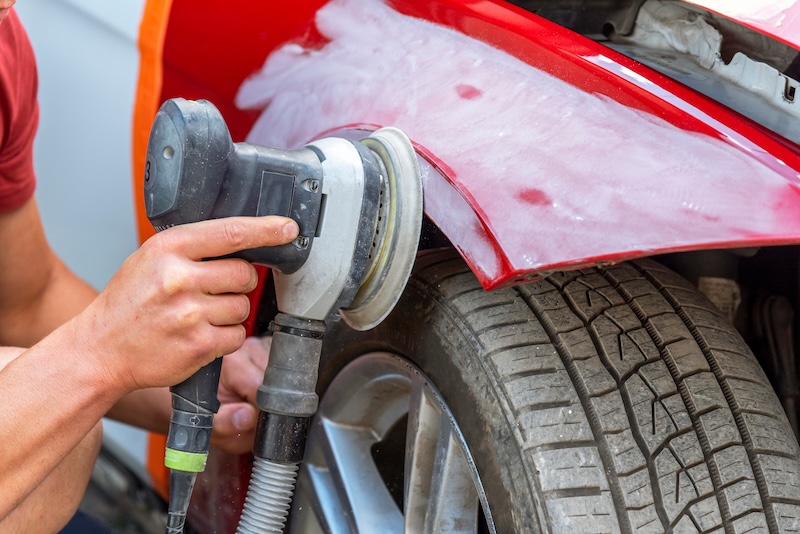 Grinder in the hands of a man who sharpen a car varnish in the car shop.