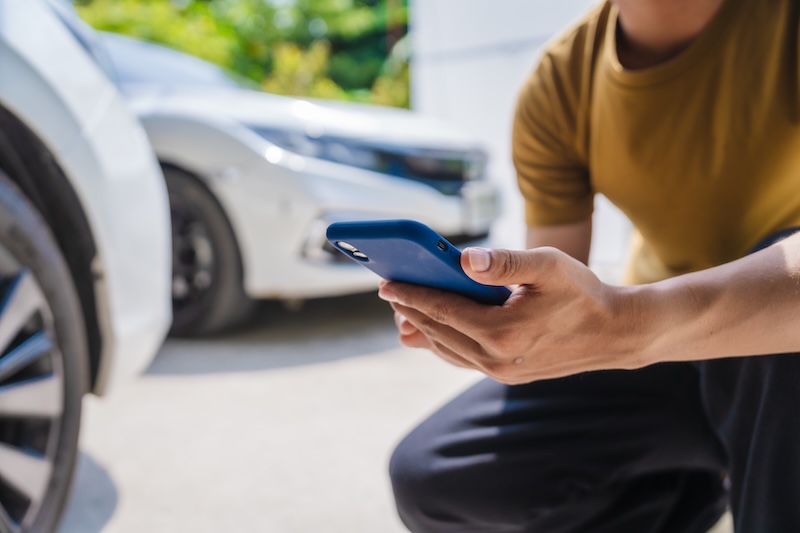 Man fills out a car insurance form after a car accident. Comprehensive motor insurance covers car damage. He files a claim report, speaking with an adjuster to understand his coverage and deductible.