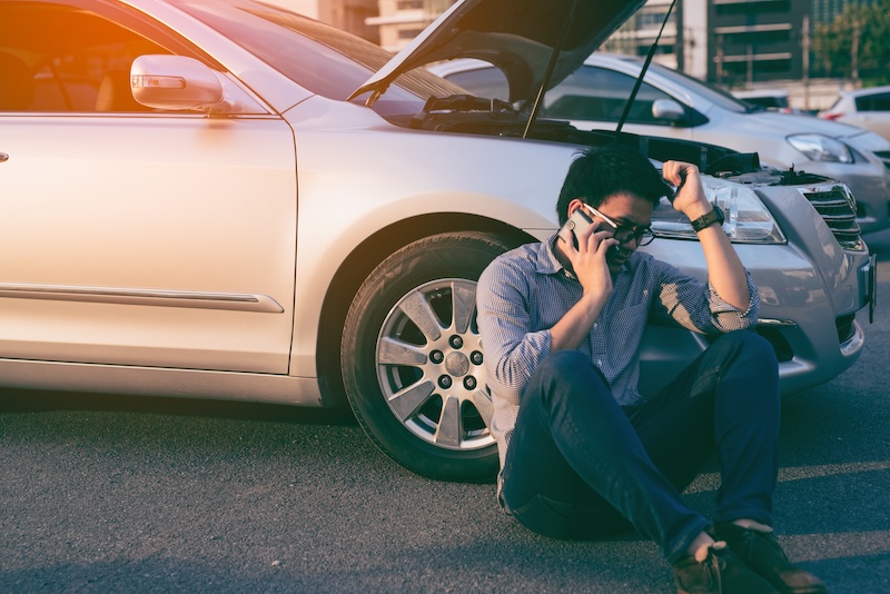 Young asian handsome man siting by the Broken Down car and calling for help with smart phone