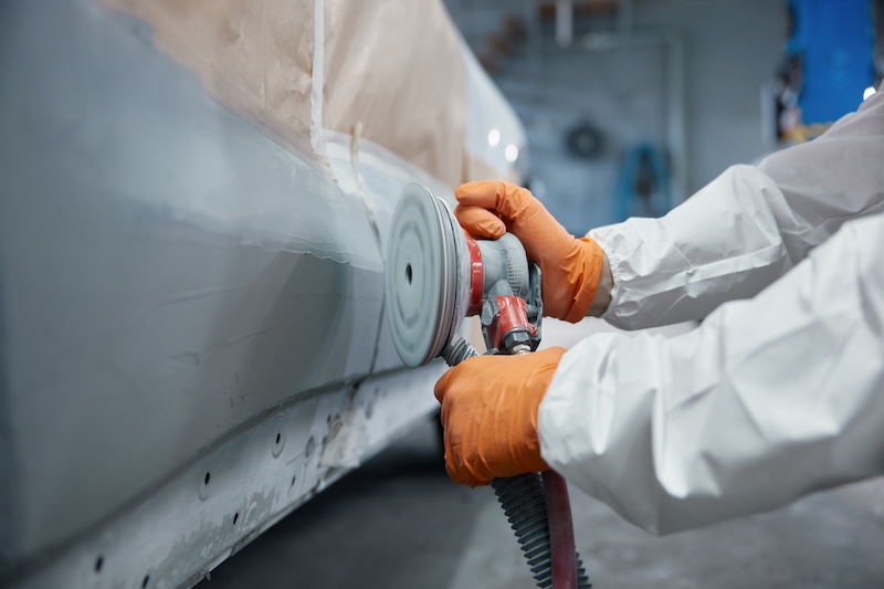 Close-up of a technician sanding a car body panel with an orbital sander, wearing protective gloves and coverall. SSUCv3H4sIAAAAAAAACoRUyY6cMBC9R8o/tDgPCgbay3xAblFyH+VQXmisNhgZM8lo1P+eAppuk/QoN+pV1avFr3j//OlwyCSMVmXPh/fZQts6N40xQLS+R7h4uuLB9NqEFHkNFS1SAGxqGW2jDxZcCkqIqu2hMwj2k3MzfFmc2RghTqMZk14UduK7Jg5HBKuNQ3nnpyD97xQcWh+9nnqzA32v51SSlFEQzQn72hXalvCy2ofNsdaDiK7sB4Tz+OX7FLX3IXtKAsZJzgHf7KiMc9AbP43Z5l/LfsRp/ODMI7Kv0Fk3N3njWT9+3pZ9Mr16u88wp7ZTjCbgztQ5HQZdpLgRbQwzh/bSPA4/HumjDB0MdGO0ywPuMlAK6RhibxLCHjbgoHv7i6lqpKplU+SVZGVeA2tyLhTNTVUSLZlhptlzV4pSzkHmDVMqrxWmckpNLghBjykLJLsXXz8uiSKCcQZW4b2svWXnX7jHblHINQgmbX2imFevwM0BVcIEdoAAu7whWGX7U4L42C53dBO5n/oY5i1k21iZ834Aicp4PjRYxmx4C+OI4XrDU10vt5LU6X1cZrqyZhqFP5ukqgvKRSV4XRaUiIJl6QG2FnmWdrYGp8F50EbvtLY7TcIoYaiYcru89PYYLbFQVdLr5rdZUOidRb3+j5cRwdmdN73+mZtwUVbHpG7yI1hqE8GO9b+vvsje6vSt7NwK7qcRgsgiL3nJ87qqIQdS1rk4NlLUglPgHOV0+QMAAP//AwBC0Rn9PwUAAA==