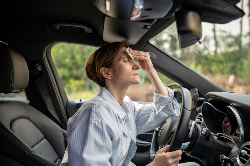 Woman drives car with broken air conditioning in hot summer weather. Wipes sweat paper napkin. Middle aged female suffering from heat stuffiness, high temperature, humidity. Overheated worried driver.