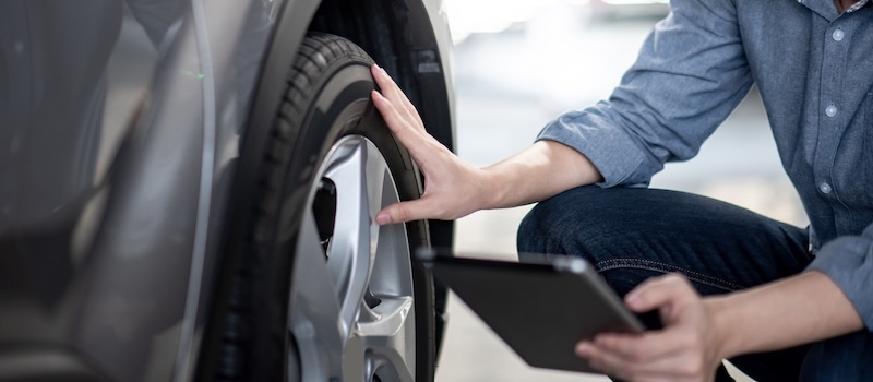 Asian auto mechanic holding digital tablet checking car wheel in auto service garage. Mechanical maintenance engineer working in automotive industry. Automobile servicing and repair concept