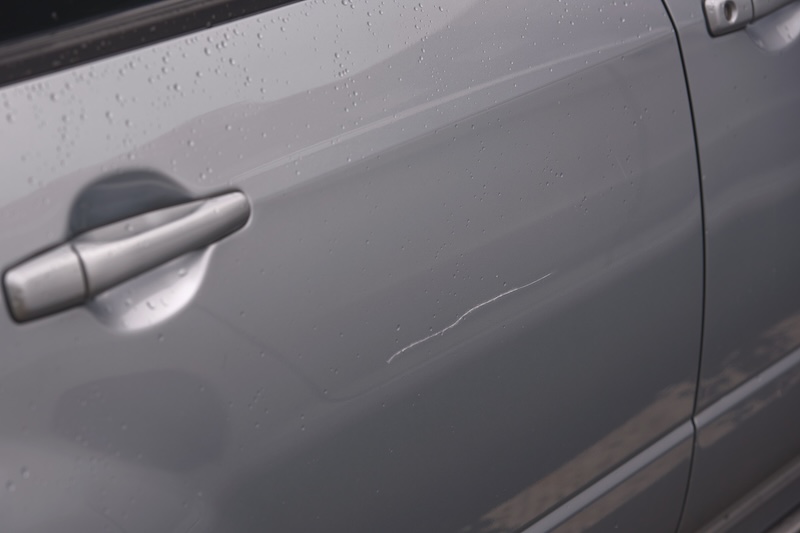 Сar door scratched, damage to paint and lacquer coat. Dent car scratch. Vandal scratched car with nail at parking lot.