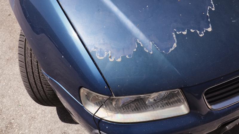 Faded car paint - peeling paint surface in a 15 year old compact blue car.