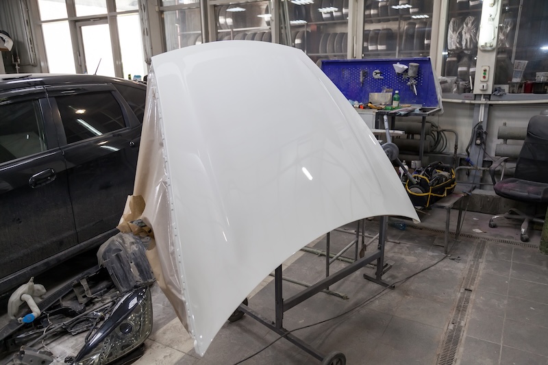Painting and drying in a professional box of car body parts after applying putty and paint hood in the body repair shop with white lanterns in the working environment. Auto service Industry.