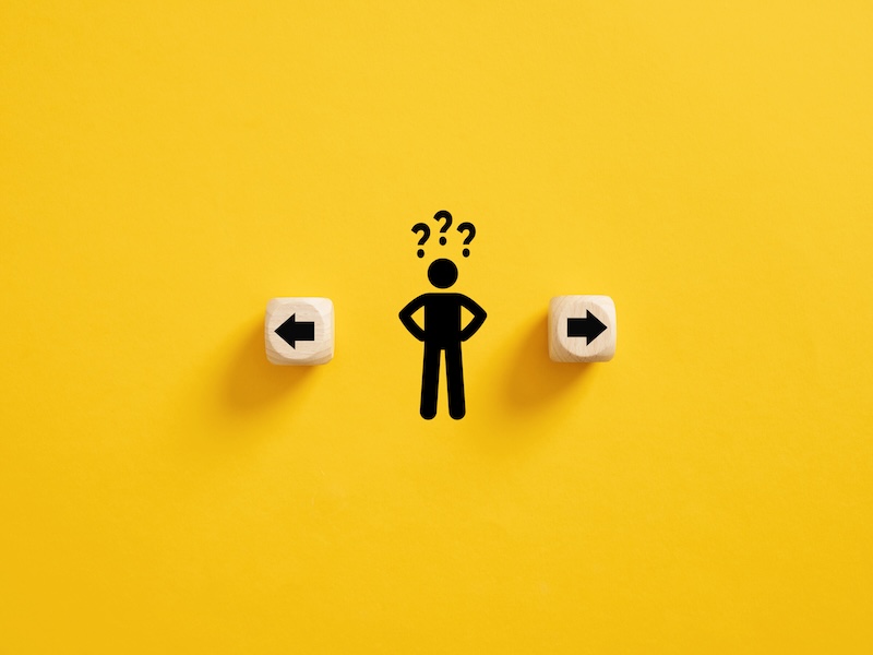 Decision making and choosing the right path. Confusion about deciding which direction to go. Stickman with question marks standing in between the wooden cubes with arrow symbols.