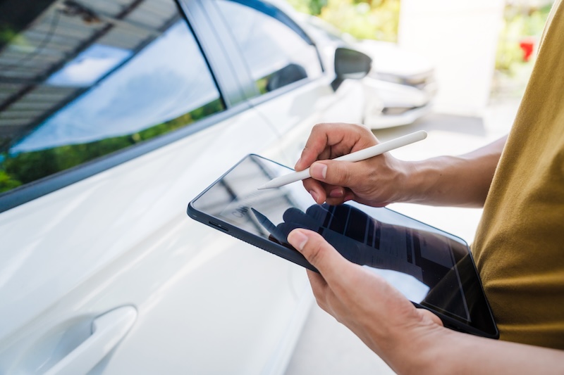 Man fills out a car insurance form after a car accident. Comprehensive motor insurance covers car damage. He files a claim report, speaking with an adjuster to understand his coverage and deductible.