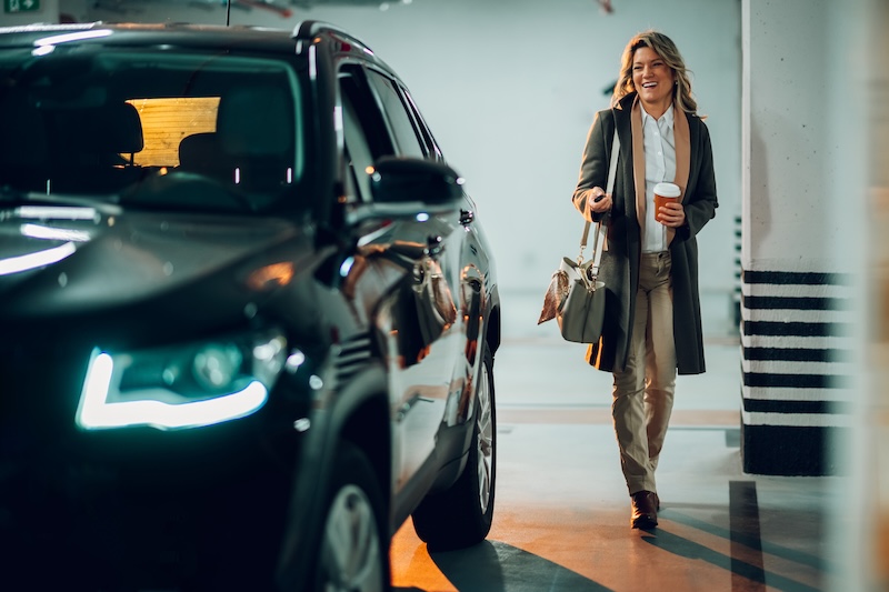 Successful businesswoman entering or exiting her car in a contemporary underground parking structure, clutching a cup of coffee and a set of car keys