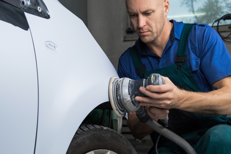 Grinder in the hands of a man who sharpen a car varnish in the car shop.