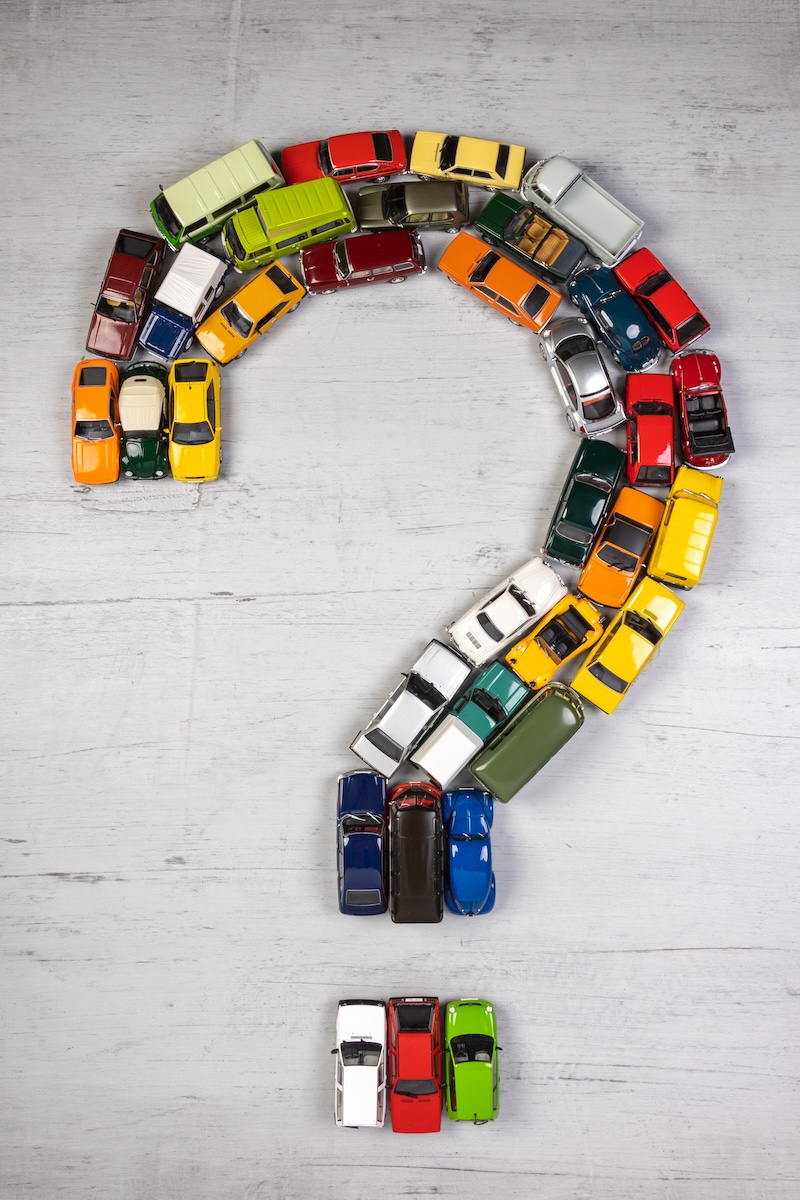 question mark, formed with toy cars, on a gray wooden board