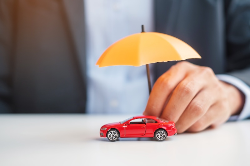 Businessman hand holding umbrella and cover  red car toy on table. Car insurance, warranty, repair, Financial, banking and money concept